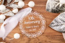 Load image into Gallery viewer, Clear Acrylic 10th Anniversary Ornament, personalized with your names and wedding year with decorative elements on a wooden surface