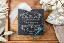 Load image into Gallery viewer, Clear Acrylic Personalized 25th anniversary ornament with engraved Names and wedding year on a wooden surface with decorative elements shown on black gift box with blue ribbon.