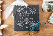 Load image into Gallery viewer, Clear Acrylic Round Personalized Anniversary Ornament with Couple's Names and wedding Year strung on a white ribbon displayed on a wood tray with decorative elements. Also displayed is a black gift box