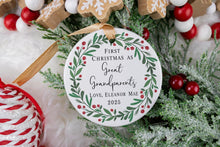 Load image into Gallery viewer, Personalized Ceramic Christmas ornament First Christmas as Great Grandparents with the baby's name and year. Adorned with a green wreath and red berries. The ornament is displayed on a table with Christmas Decorations.
