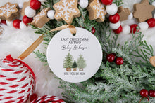 Load image into Gallery viewer, Personalized Christmas ornament made from white ceramic that says last Christmas as two with the baby's last name with two big trees and one little tree. the bottom says see you in the year the baby is to be born. The ornament is displayed on a christmas wreath with red and white ornaments.