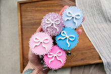 Load image into Gallery viewer, Four colorful scalloped acrylic badge reels with raised bows, displayed together in a hand.