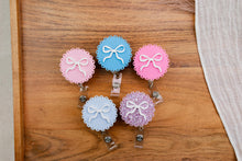 Load image into Gallery viewer, Five round acrylic badge reels with scalloped edges and white bow decorations on a wooden tray.