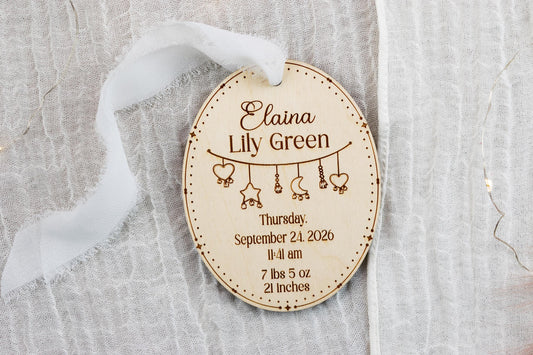 Personalized oval wooden baby birth announcement ornament with engraved name, birth statistics, and white ribbon hanger.