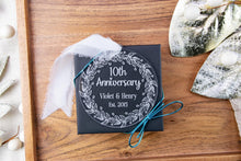 Load image into Gallery viewer, Clear Acrylic 10th Anniversary Ornament, personalized with your names and wedding year with decorative elements on a wooden surface


