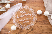 Load image into Gallery viewer, Clear Acrylic 10th Anniversary Ornament, personalized with your names and wedding year with decorative elements on a wooden surface
