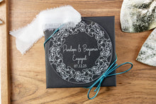 Load image into Gallery viewer, Clear acrylic round engagement ornament on engraved with names and engagement date with thick floral wreath. Displayed on a wooden tray. 
