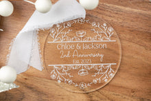Load image into Gallery viewer, Clear Acrylic Round Personalized Anniversary Ornament with Couple's Names and wedding Year  strung on a white ribbon displayed on a wood tray with decorative elements. 
