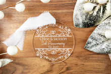 Load image into Gallery viewer, Clear Acrylic Round Personalized Anniversary Ornament with Couple's Names and wedding Year  strung on a white ribbon displayed on a wood tray with decorative elements. 

