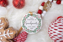 Load image into Gallery viewer, Personalized Ceramic Christmas ornament First Christmas as Grandparents with the baby's name and year. Adorned with a green wreath and red berries. The ornament is displayed on a table with Christmas Decorations. 
