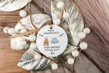 Load image into Gallery viewer, Personalized ornament for first grandchild with a brown pair of pants and blue sweater on a clothes line. Displaying the baby's last name and due year. The product is displayed on a wooden tray with decorative elements.
