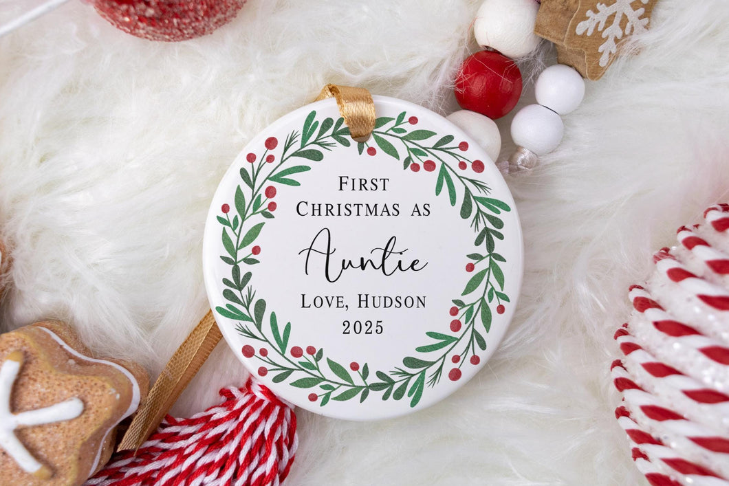Personalized Christmas ornament with 'First Christmas as Auntie' text, surrounded by festive decorations on a white background.