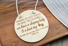 Load image into Gallery viewer, Natural birch wood door sign with engraved sleeping baby and loud dog message, shown hanging by cotton rope.

