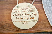 Load image into Gallery viewer, Round birch wood hanging sign engraved with a message about a sleeping baby, loud dog, and leaving deliveries at the door.
