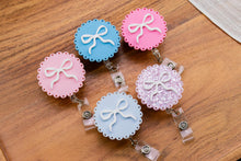 Load image into Gallery viewer, Overhead angled view of five scalloped acrylic badge reels in blue and pink shades.
