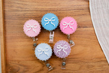 Load image into Gallery viewer, Five scalloped acrylic bow badge reels with retractable clips displayed together.
