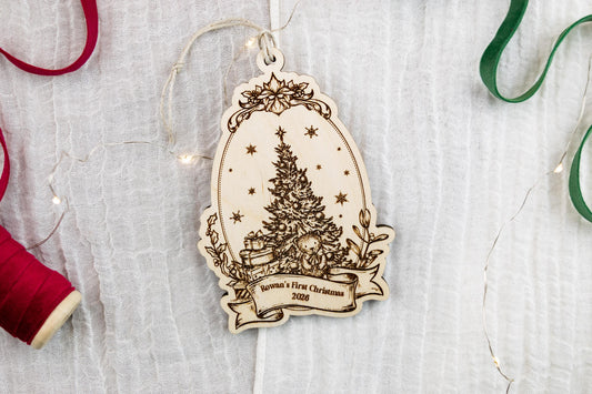 Wooden Christmas ornament with decorative floral frame, vintage Christmas tree, and banner reading Rowan's First Christmas 2026.