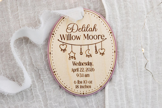 Oval wood baby birth stats ornament with pink acrylic backing, engraved with Delilah Willow Moore, birth details, and hanging charms.