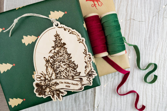 Vintage wooden Christmas ornament with engraved tree, woodland animals, greenery, and a banner reading The Miller Family 2026.